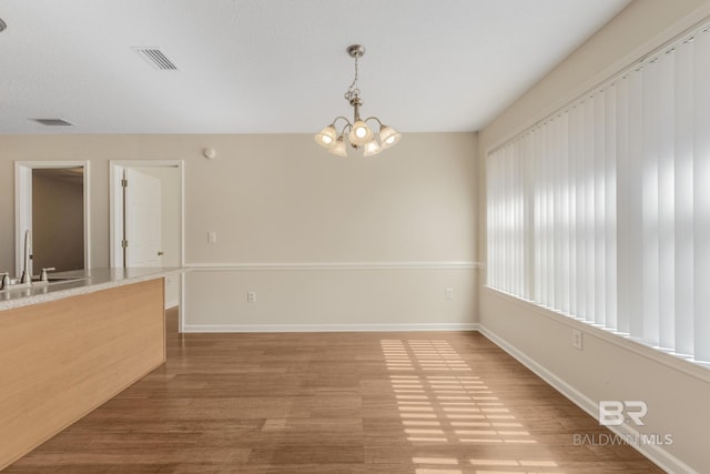 unfurnished dining area with visible vents, a sink, wood finished floors, a chandelier, and baseboards