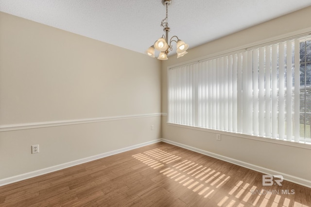 unfurnished room with a textured ceiling, baseboards, a notable chandelier, and wood finished floors