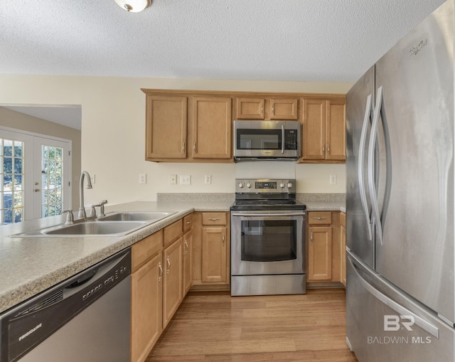 kitchen featuring light wood finished floors, light countertops, appliances with stainless steel finishes, and a sink