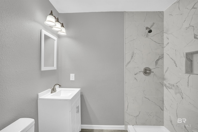 bathroom with a tile shower, vanity, and toilet