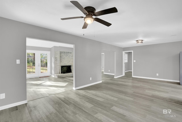 unfurnished living room featuring french doors, light hardwood / wood-style floors, a brick fireplace, and ceiling fan