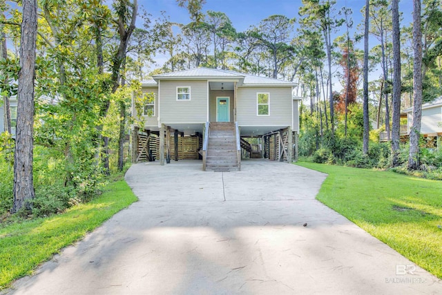 raised beach house featuring stairway, driveway, a carport, a front lawn, and metal roof