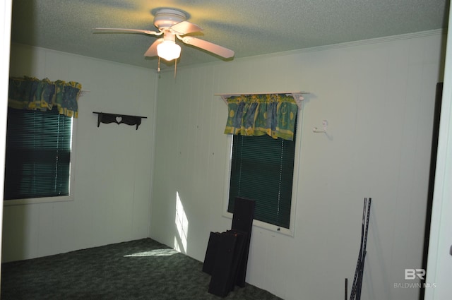 empty room featuring dark colored carpet, a textured ceiling, ceiling fan, and ornamental molding