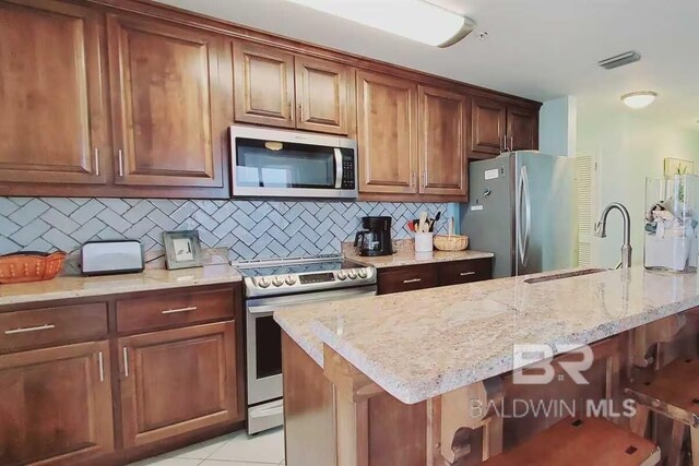 kitchen featuring appliances with stainless steel finishes, light stone countertops, sink, tasteful backsplash, and a breakfast bar