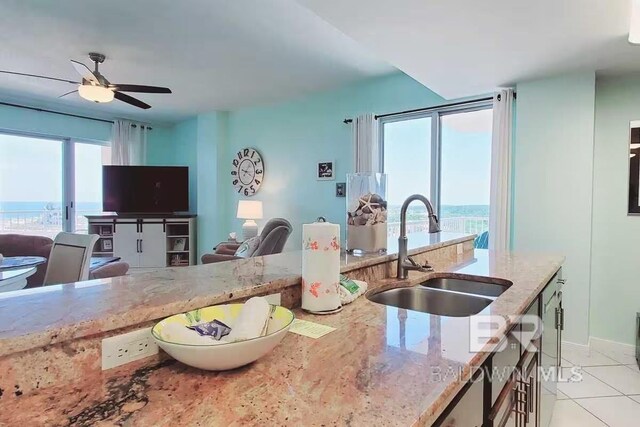 kitchen with light tile patterned floors, light stone counters, sink, and ceiling fan