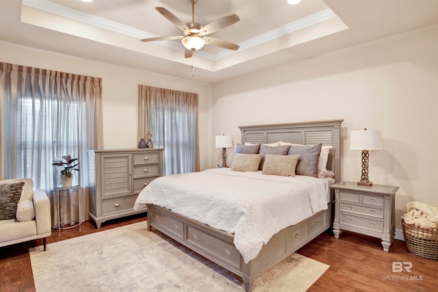 bedroom with hardwood / wood-style flooring, a raised ceiling, and ceiling fan