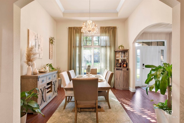 dining area featuring dark wood-type flooring, a notable chandelier, ornamental molding, and a raised ceiling