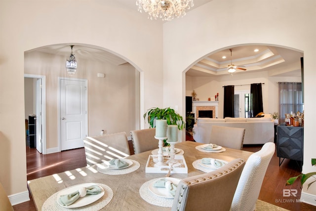 dining area with dark wood-type flooring, a high ceiling, ceiling fan with notable chandelier, and a raised ceiling