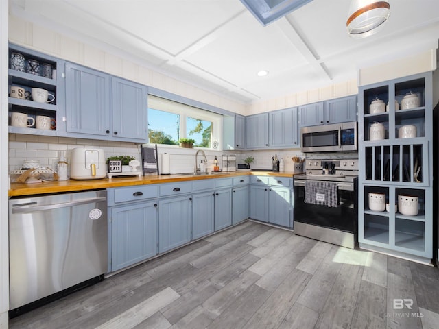 kitchen with blue cabinets, butcher block counters, sink, stainless steel appliances, and light hardwood / wood-style floors