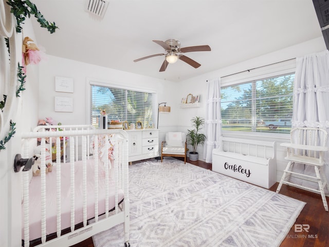 bedroom with a nursery area, ceiling fan, and dark hardwood / wood-style flooring