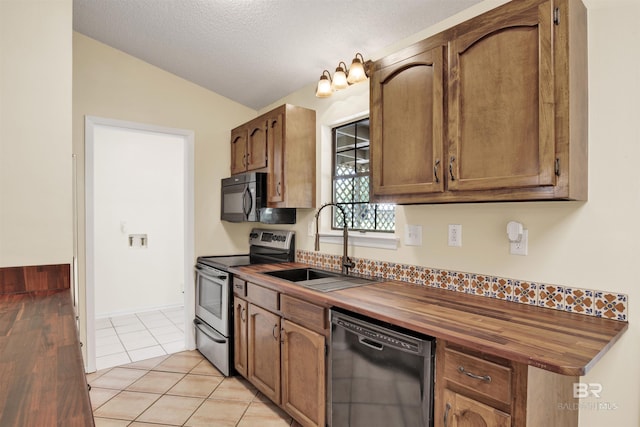 kitchen featuring lofted ceiling, black appliances, sink, light tile patterned floors, and butcher block counters