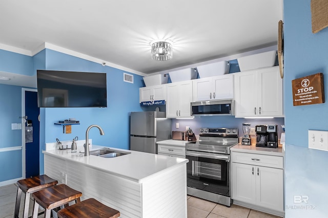 kitchen featuring light tile patterned floors, appliances with stainless steel finishes, a kitchen bar, sink, and white cabinetry