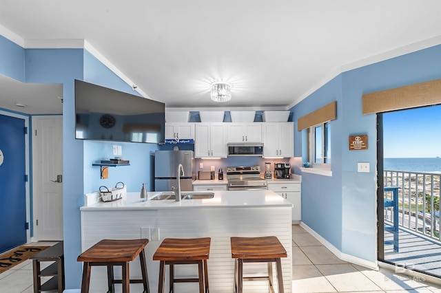 kitchen featuring a breakfast bar, a sink, white cabinets, a peninsula, and appliances with stainless steel finishes