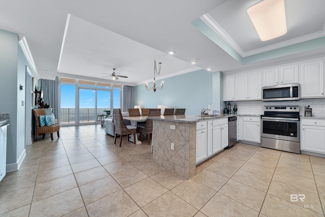 kitchen featuring appliances with stainless steel finishes, light stone countertops, ornamental molding, white cabinets, and kitchen peninsula