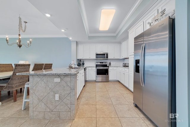 kitchen featuring stainless steel appliances, a kitchen bar, a raised ceiling, and white cabinets