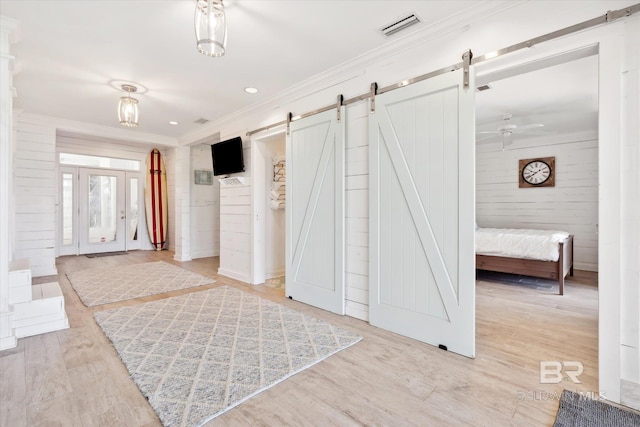 interior space featuring a barn door, wooden walls, light hardwood / wood-style floors, and ornamental molding