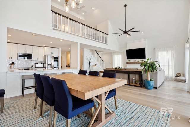 dining room with ceiling fan, light hardwood / wood-style floors, and high vaulted ceiling