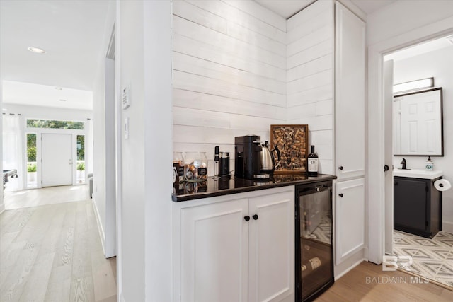 bar featuring white cabinets, light hardwood / wood-style flooring, and wine cooler