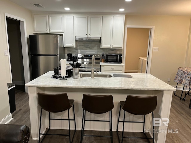 kitchen with appliances with stainless steel finishes, a kitchen island with sink, white cabinets, and washer and clothes dryer