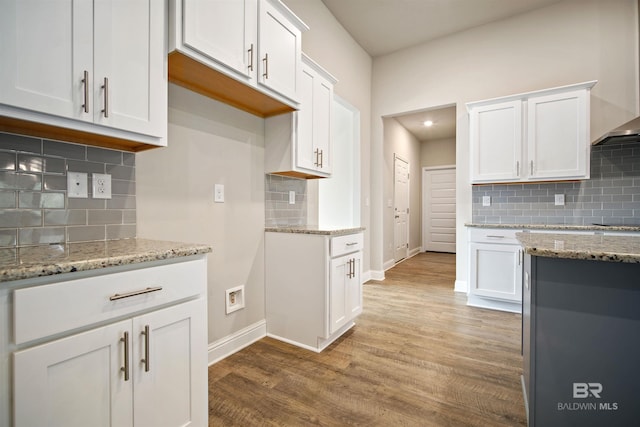 kitchen featuring wood-type flooring, decorative backsplash, white cabinets, wall chimney exhaust hood, and light stone counters