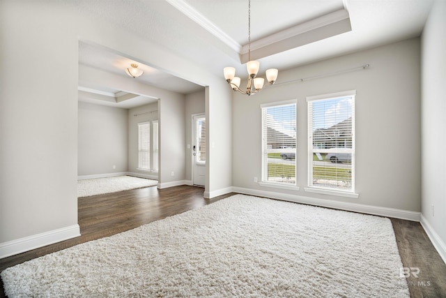 unfurnished room with dark wood-type flooring, an inviting chandelier, ornamental molding, and a tray ceiling