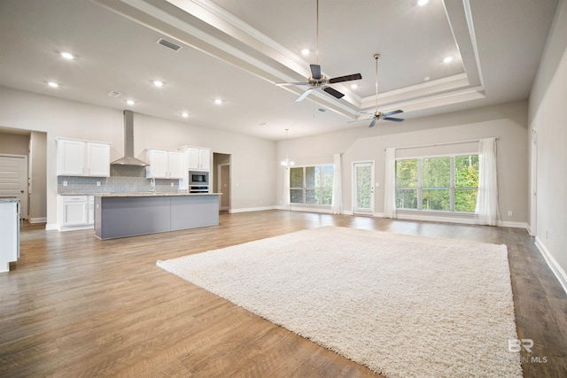 unfurnished living room featuring ceiling fan with notable chandelier, a high ceiling, a raised ceiling, light wood-type flooring, and crown molding