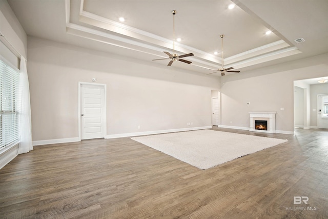 unfurnished living room featuring ceiling fan, wood-type flooring, a tray ceiling, and ornamental molding