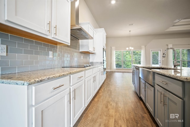 kitchen featuring light stone countertops, white cabinetry, pendant lighting, and wall chimney range hood