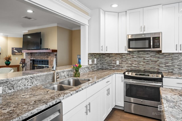 kitchen with a sink, appliances with stainless steel finishes, a brick fireplace, tasteful backsplash, and crown molding