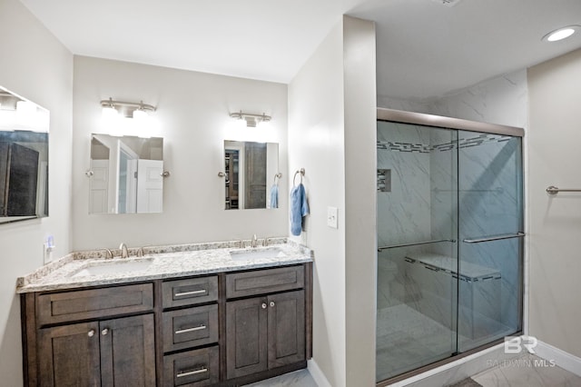 full bath with double vanity, a marble finish shower, baseboards, and a sink