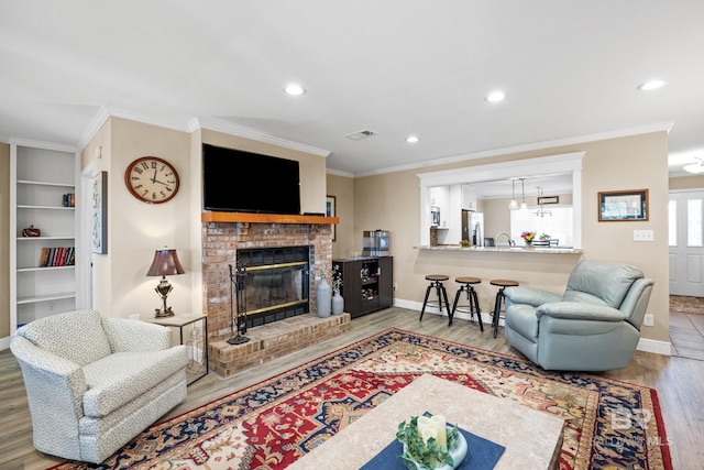 living area with ornamental molding, a brick fireplace, wood finished floors, and visible vents