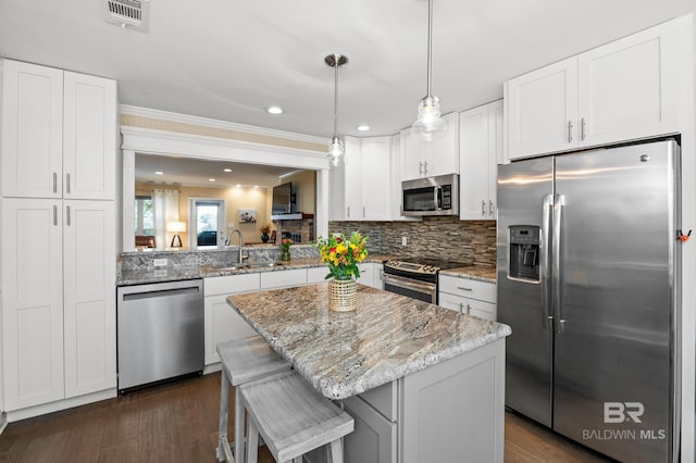 kitchen featuring stainless steel appliances, a kitchen island, a sink, visible vents, and light stone countertops