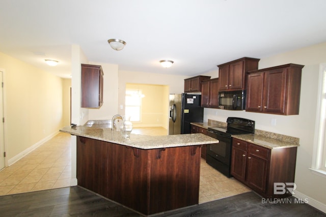 kitchen with sink, a kitchen bar, black appliances, light tile patterned flooring, and kitchen peninsula