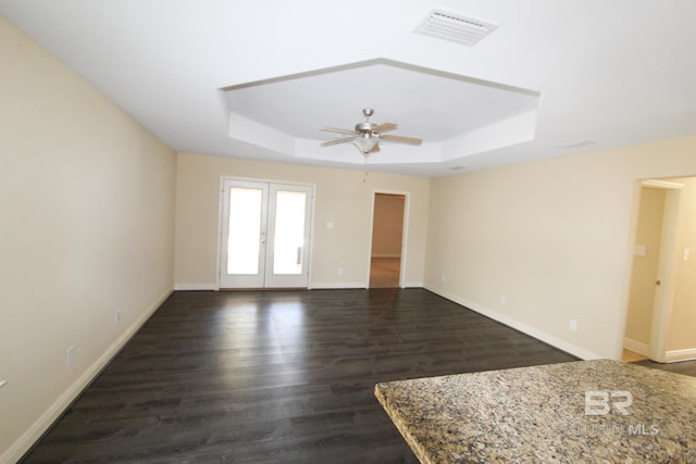 empty room with dark wood-type flooring, ceiling fan, a raised ceiling, and french doors