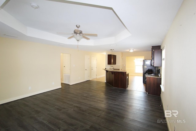 unfurnished living room with a tray ceiling, dark wood-type flooring, and ceiling fan