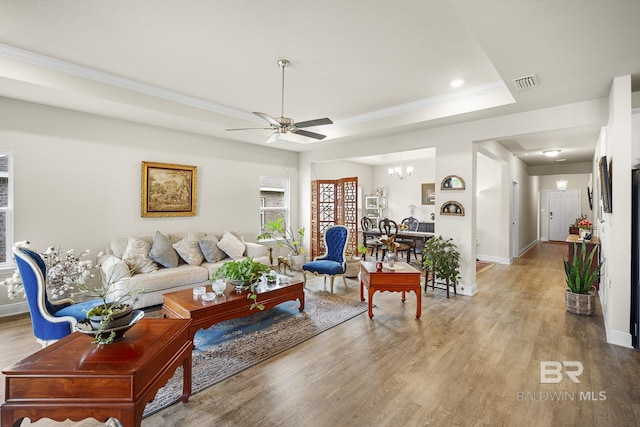 living room with ornamental molding, wood-type flooring, a tray ceiling, and ceiling fan with notable chandelier