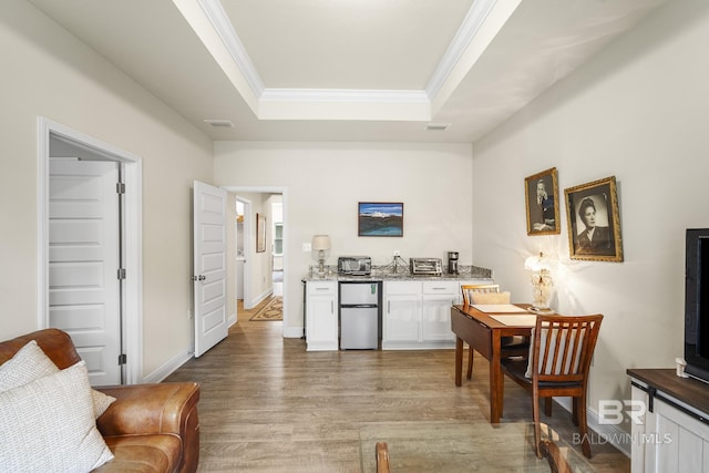 kitchen with hardwood / wood-style flooring, stainless steel refrigerator, a tray ceiling, ornamental molding, and white cabinets