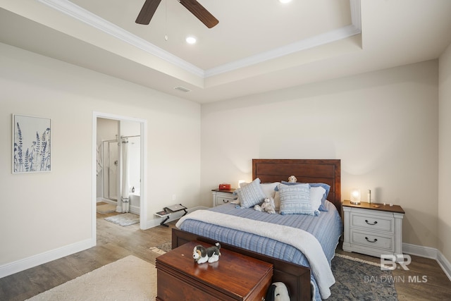 bedroom featuring a tray ceiling, hardwood / wood-style flooring, ceiling fan, and ensuite bathroom