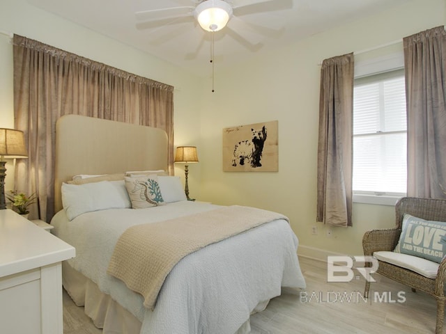 bedroom featuring light wood finished floors, multiple windows, baseboards, and ceiling fan