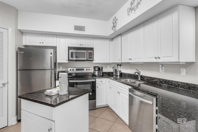 kitchen with stainless steel appliances, dark stone counters, white cabinets, sink, and light tile patterned floors