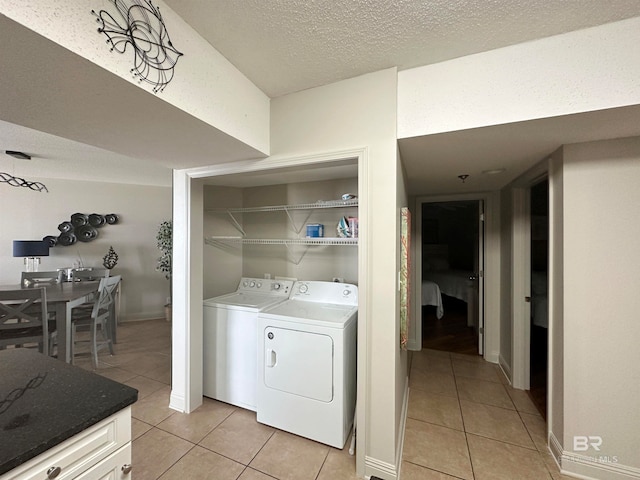 clothes washing area with a textured ceiling, washer and dryer, and light tile patterned floors