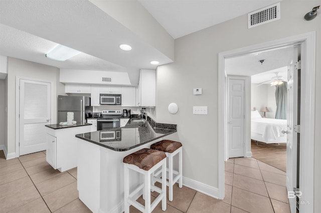 kitchen featuring stainless steel appliances, a kitchen bar, light tile patterned floors, white cabinets, and kitchen peninsula