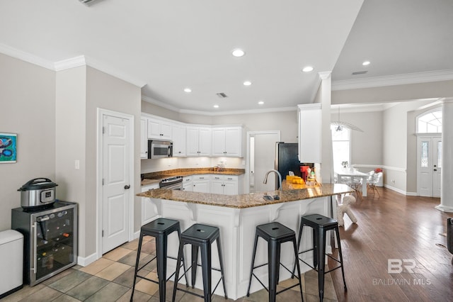 kitchen with a kitchen bar, kitchen peninsula, appliances with stainless steel finishes, beverage cooler, and white cabinets