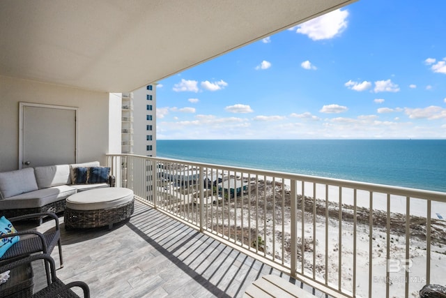 balcony with an outdoor living space, a water view, and a view of the beach