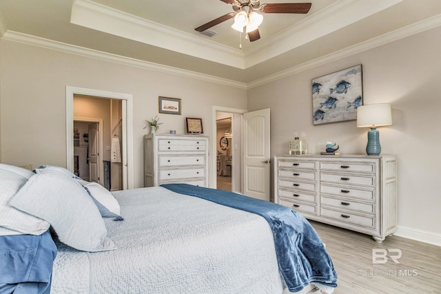 bedroom with ornamental molding, a tray ceiling, connected bathroom, and light hardwood / wood-style floors