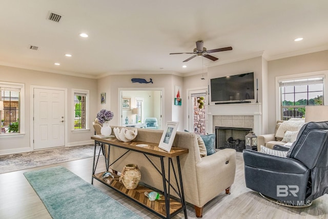 living room featuring ornamental molding, ceiling fan, a fireplace, and light hardwood / wood-style flooring