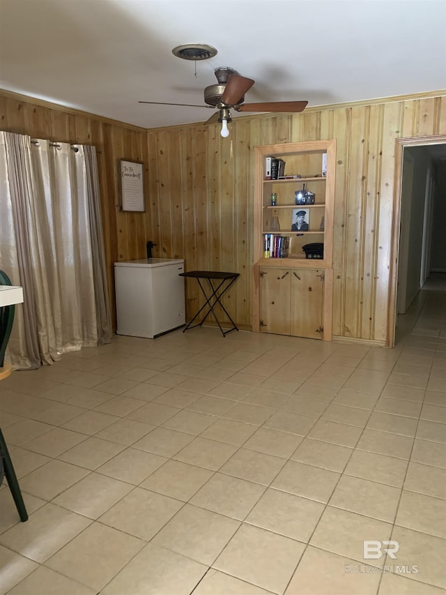 unfurnished room with wooden walls, light tile patterned floors, and ceiling fan