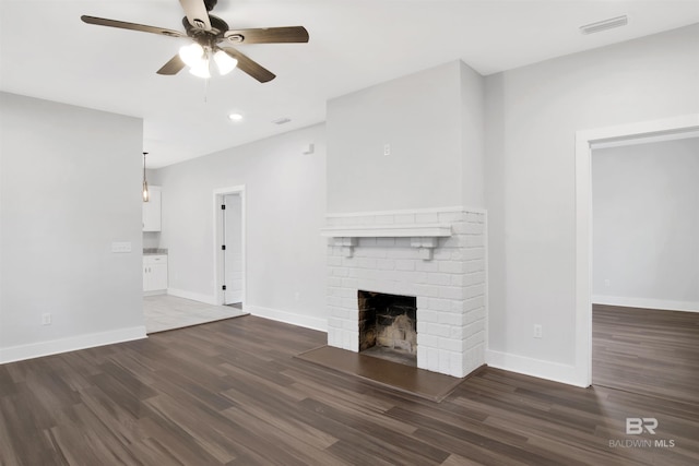 unfurnished living room featuring a brick fireplace, dark wood-type flooring, and ceiling fan