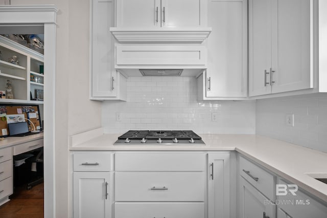 kitchen with custom exhaust hood, hardwood / wood-style flooring, backsplash, stainless steel gas cooktop, and white cabinets