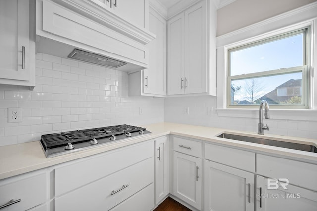 kitchen with white cabinetry, custom exhaust hood, decorative backsplash, stainless steel gas cooktop, and sink